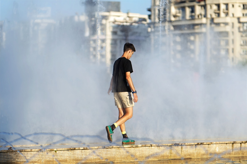 18 - A young man walking along the edge of a water basin amid rising mists from artesian fountains on a hot day